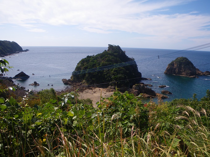 妙見浦展望所から、横長長方形の縦横３つずつの九分割の中央部分に妙見岩を捉えた構図で、全体を横断するように３本の太い青色の電線が写っている写真