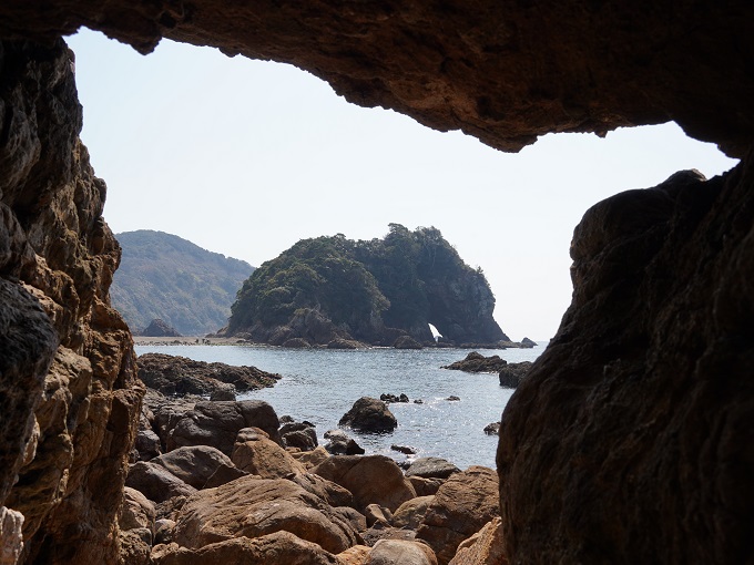 折り重なる岩の隙間から妙見岩を撮影した写真で、上下左右の手前の岩がフレームのように、中央の妙見岩が、頭を左側に向けて、座っているように見える写真